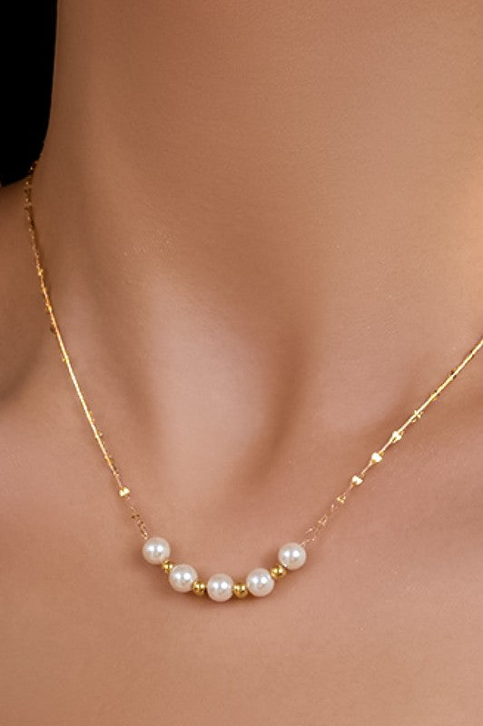 A close-up image of a woman wearing a delicate pearl necklace with gold accents.