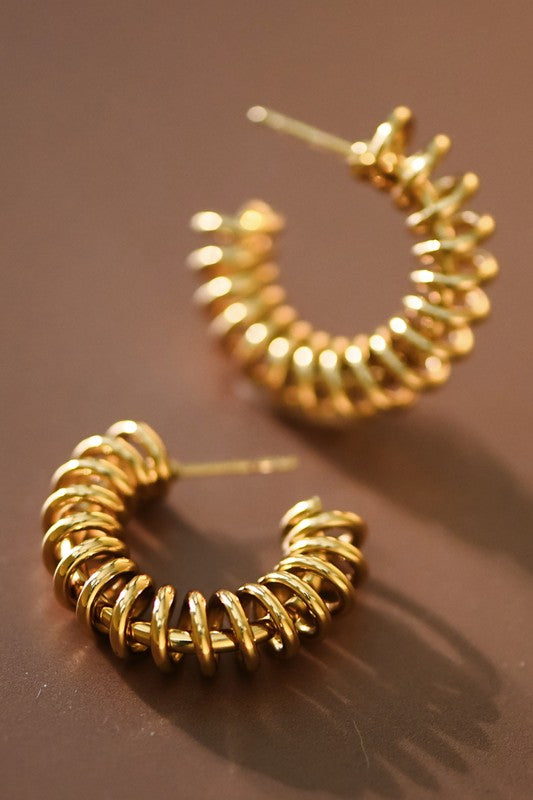 A pair of gold-plated stainless steel spiral hoop earrings on a brown surface.
