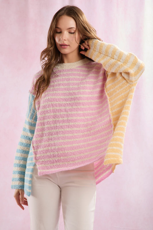 A female model wearing a pastel striped sweater with long sleeves, in a color palette that includes shades of pink, blue, and yellow.