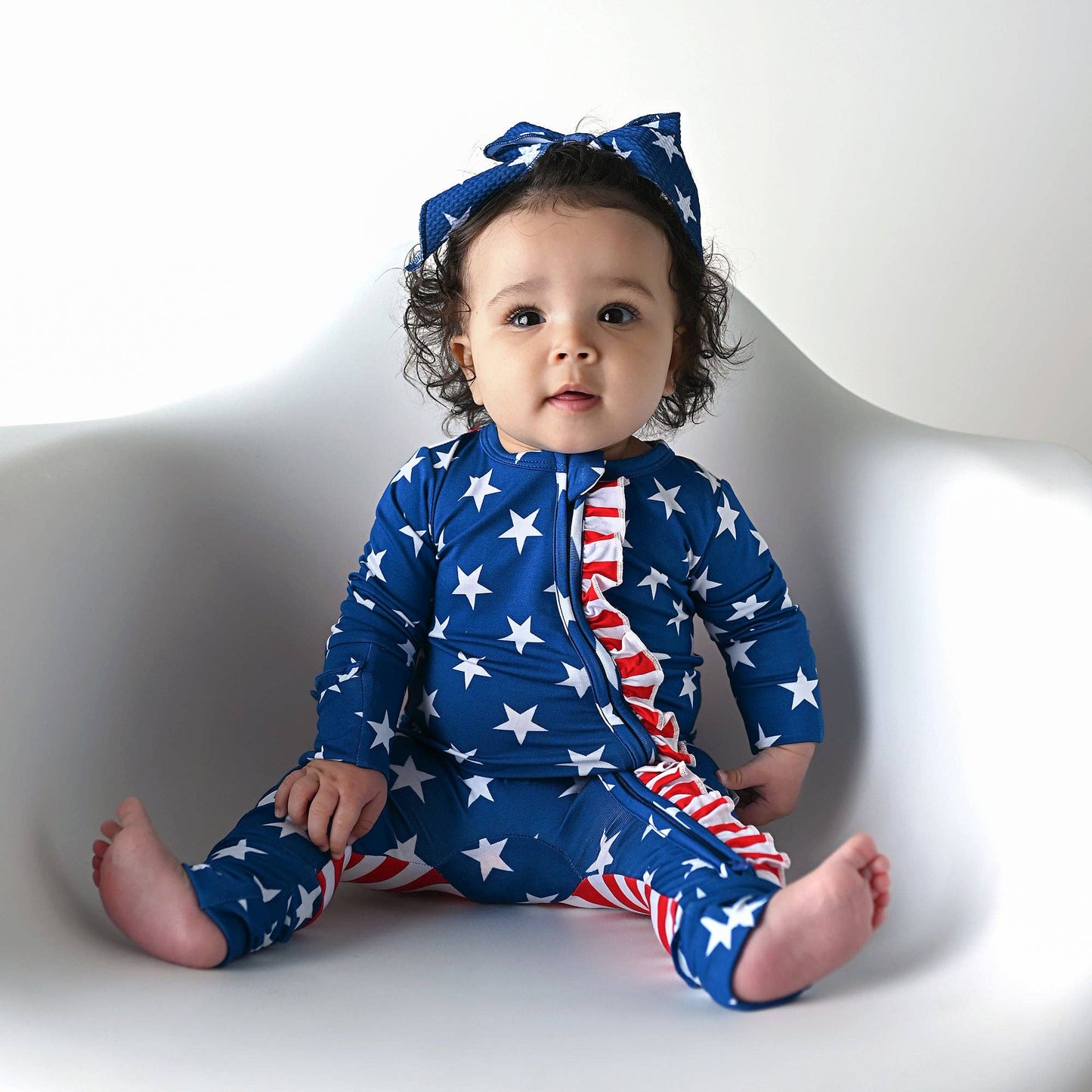 a baby sitting on a white chair wearing a patriotic outfit