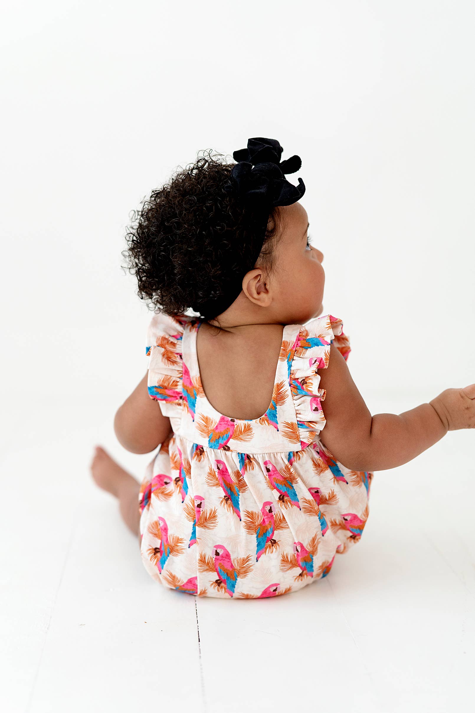 a baby girl sitting on the floor with a black bow in her hair