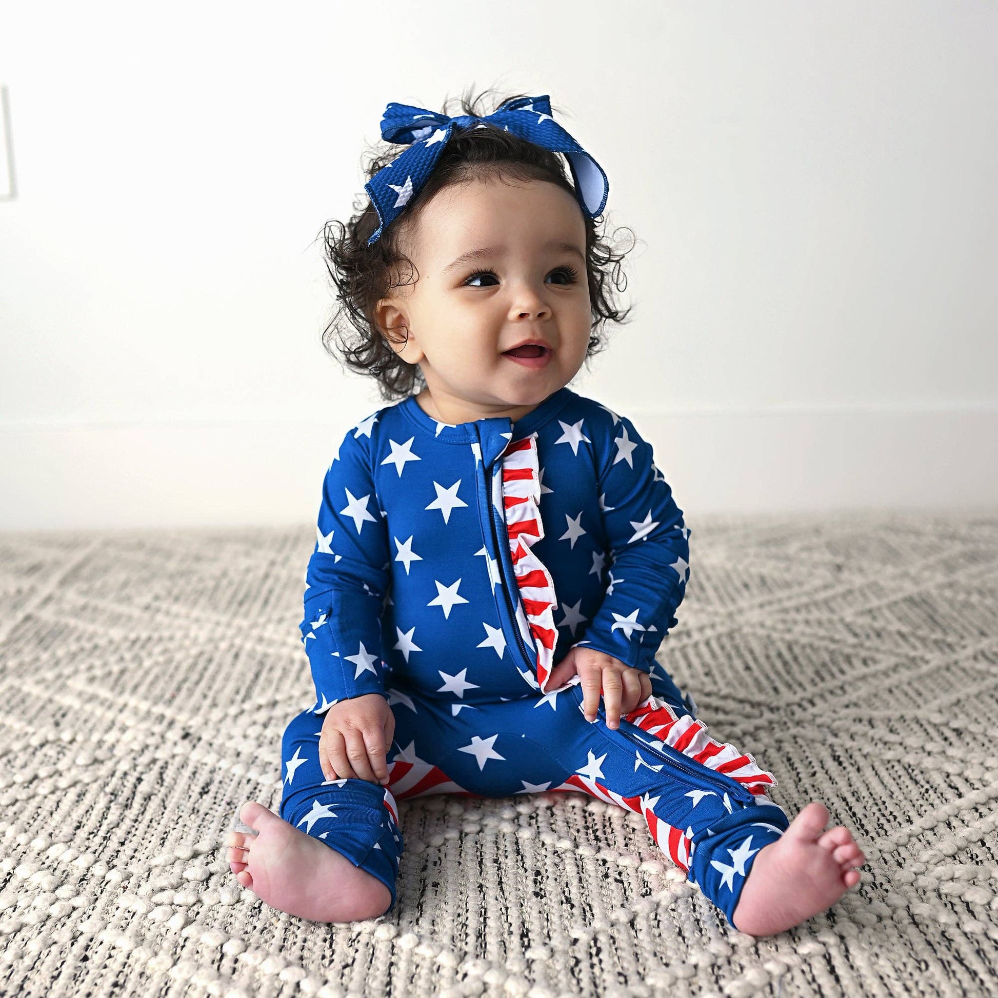 a baby sitting on a bed wearing a patriotic outfit