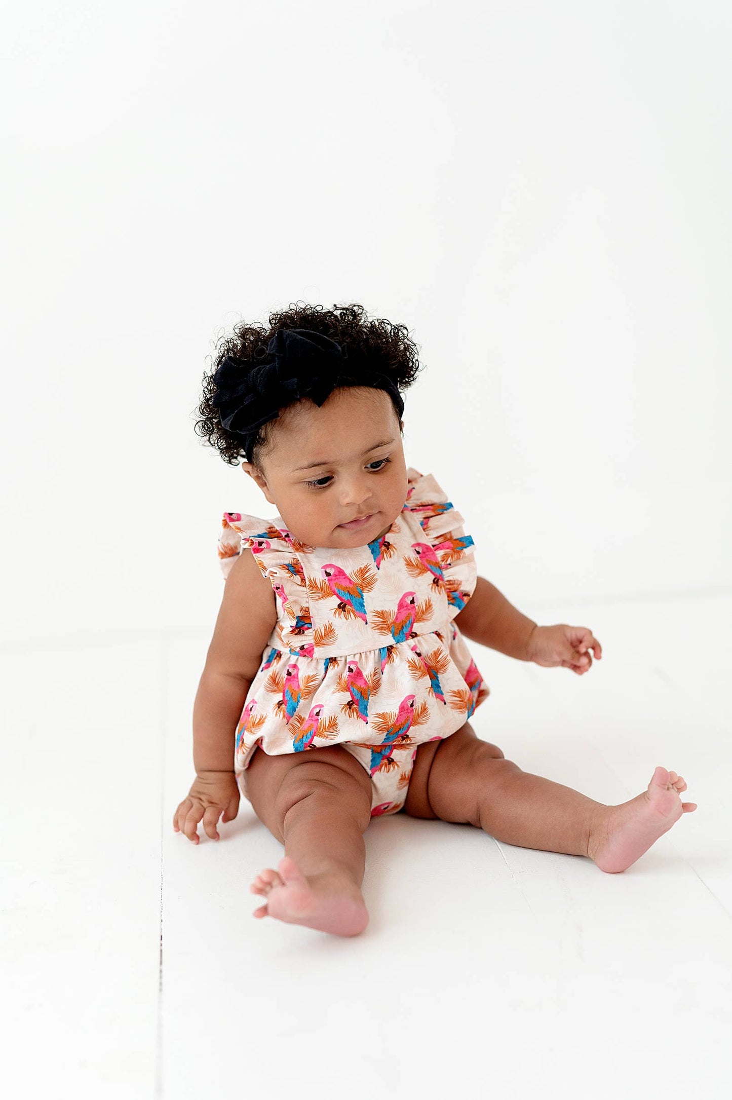 a baby girl sitting on the ground wearing a dress