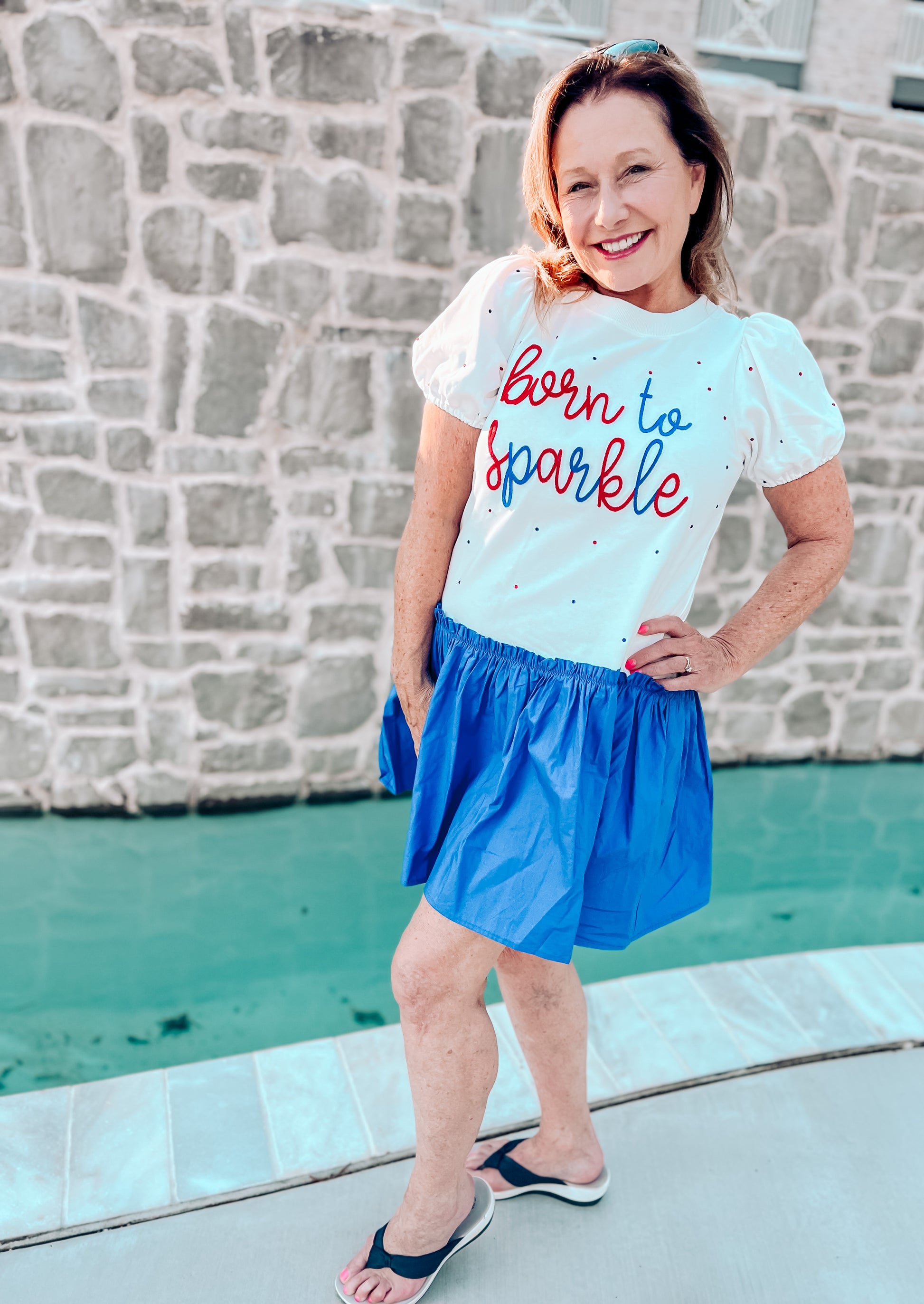 a woman standing in front of a pool wearing a shirt that says born to sparkle