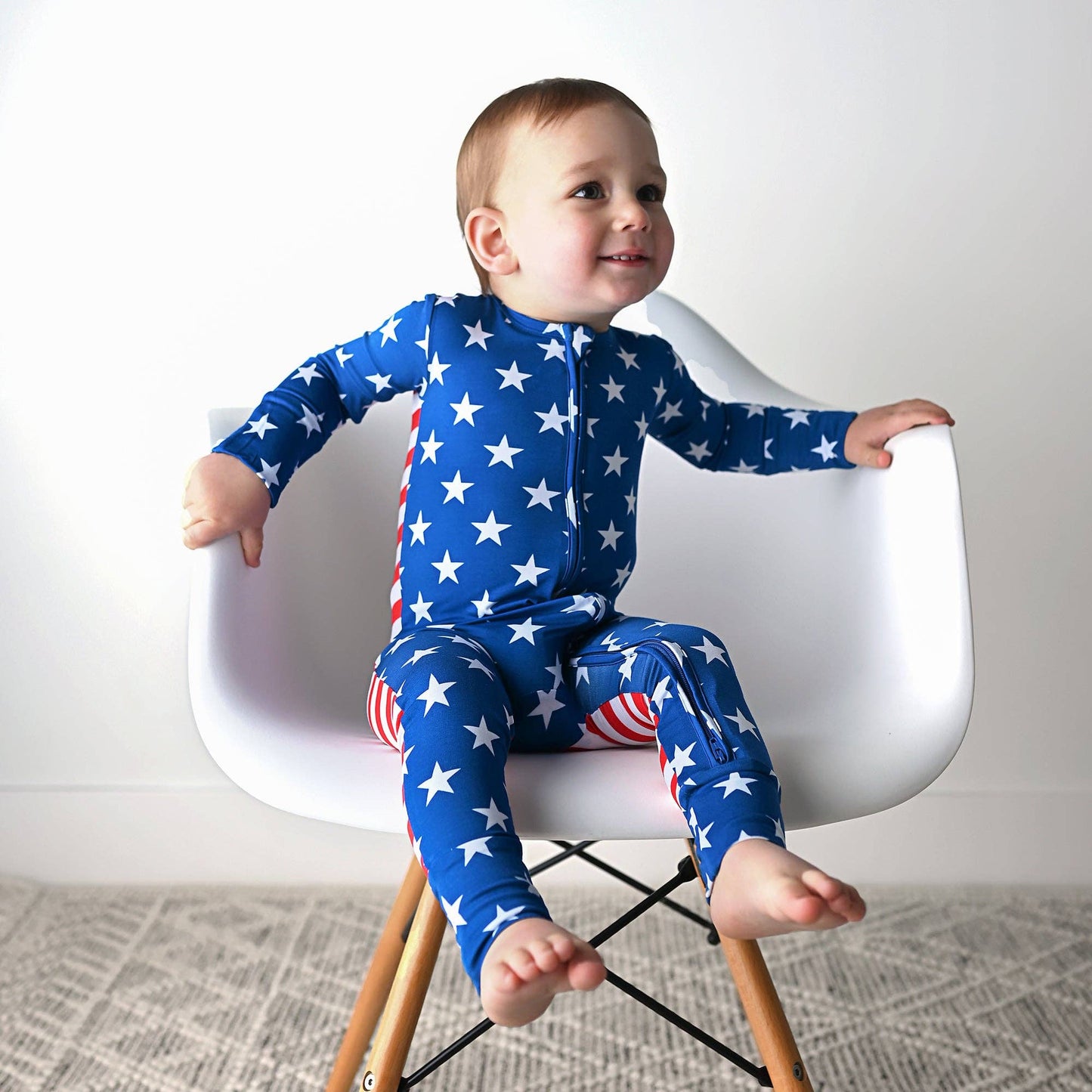 a baby sitting on a white chair with a red, white, and blue pajamas