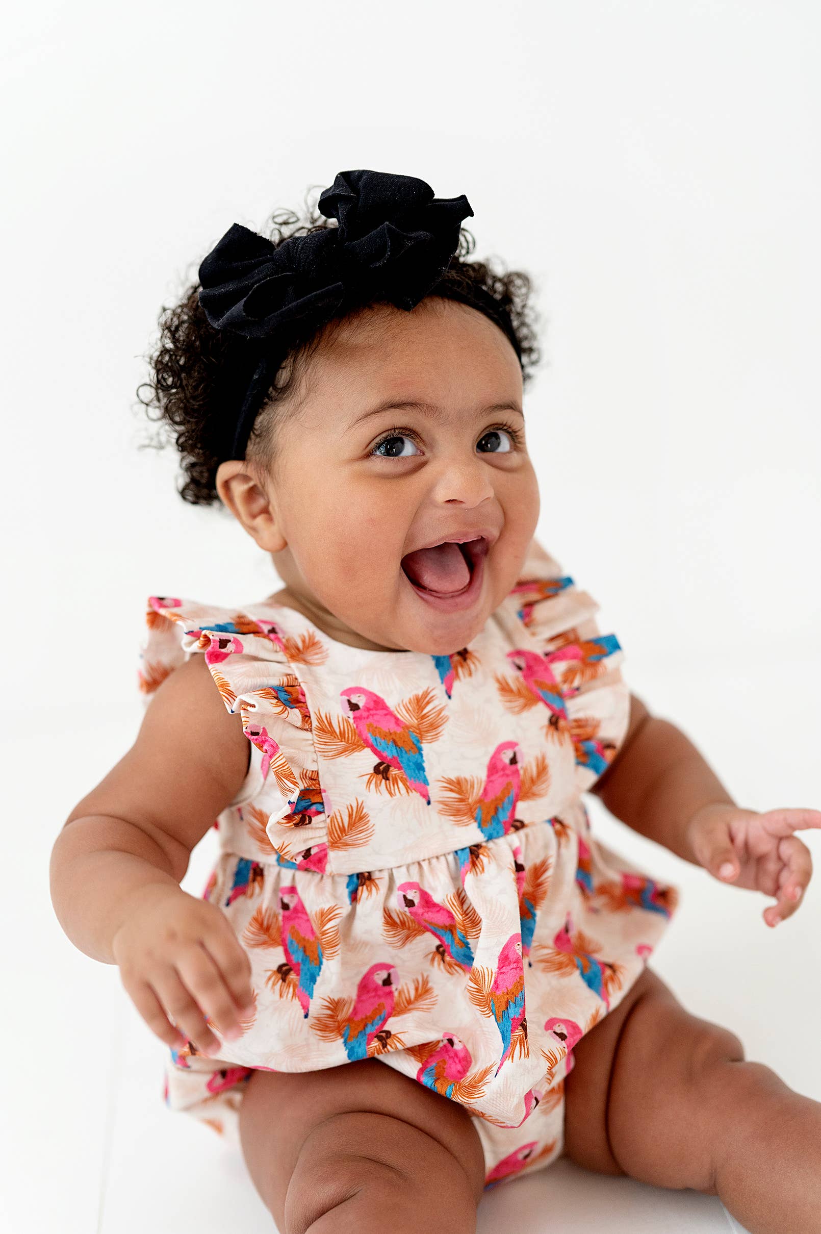 a baby sitting on a white surface with a black bow in her hair