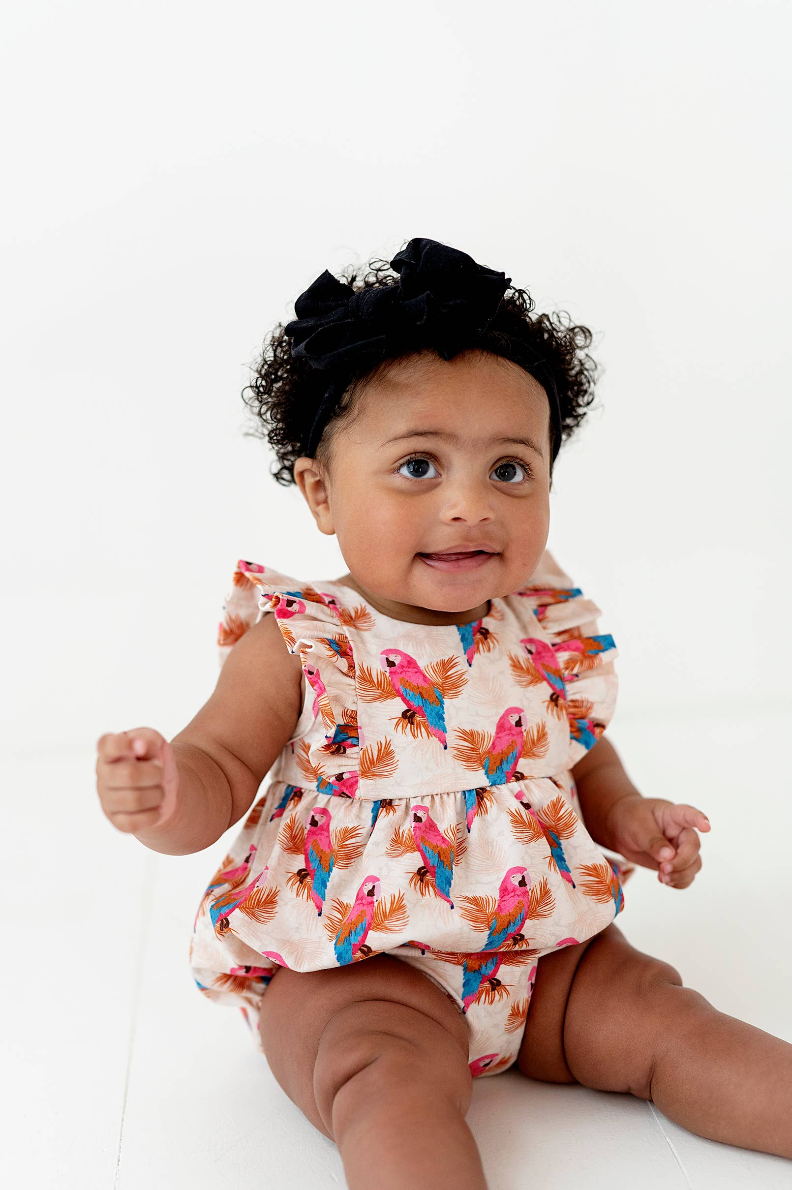 a baby girl sitting on the ground wearing a dress