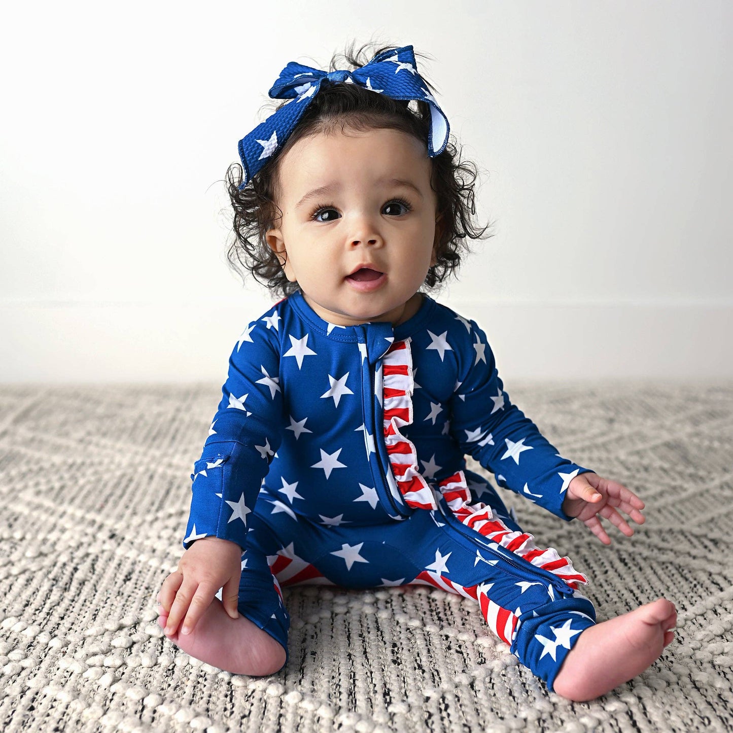 a baby sitting on the floor wearing a blue and red outfit